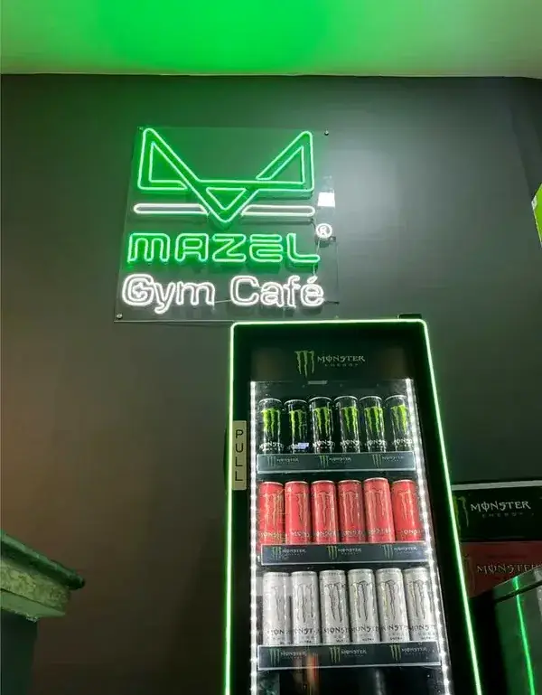 The green neon Mazel Gym Caf&eacute; sign above a drinks fridge